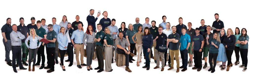 In this professional photo the teams from the UK, USA and Canadian sites are stood together in a jumbled line of different poses. All are wearing a variation of the Charles Faram branded uniform whether it be tshirts, polos or shirts. They all look casual, relaxed and friendly.