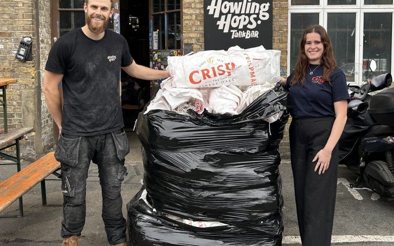 This image shows Ellie Wood Sustainability Manager from Crisp Malt and Sam Wright from Howling hops - standing next to a pack of malt bags that are being recycled by Crisp's Return a bag scheme.